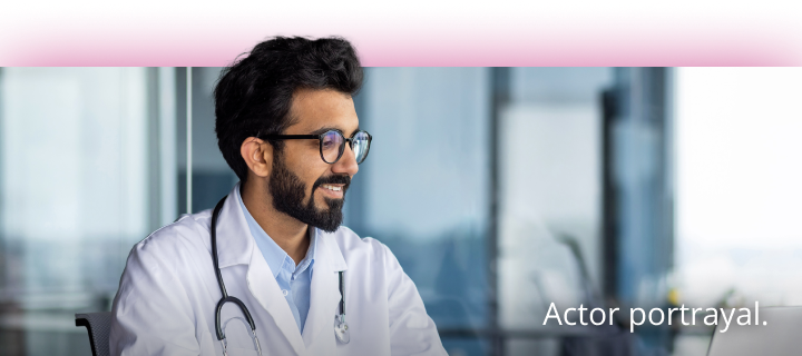 A healthcare professional looking at a laptop wearing a white coat with a stethoscope around his neck. 